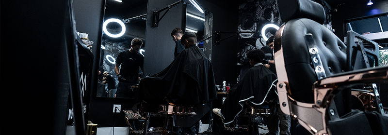 Interior of Montana Fades barbershop in Oakville, Ontario, showing a barber cutting a client’s hair at a modern styling station with ring-light mirrors and premium barber chairs.