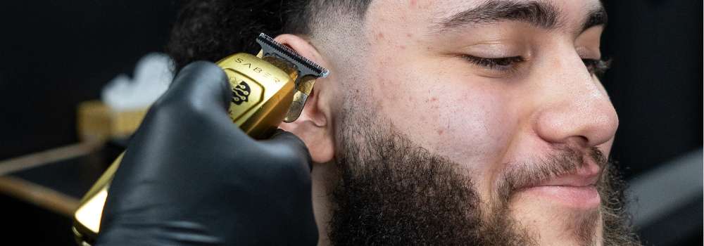 Professional barber trimming man's beard fade with gold clippers at Montana Fades barbershop in Oakville, demonstrating precision beard grooming and fade haircut coordination techniques.