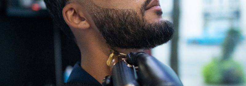 Barber at Montana Fades in Oakville, Ontario using a gold clipper to precisely shape a client’s beard along the jawline.