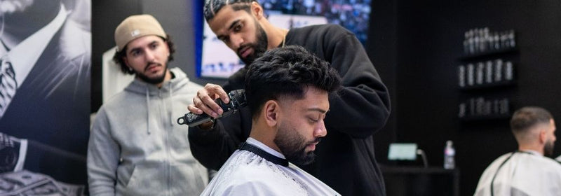 Barber at Montana Fades in Oakville, Ontario using clippers to create a precise mid fade on a seated client, with other barbers and clients visible in the sleek, modern shop.