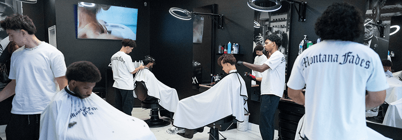 Interior of Montana Fades in Oakville, Ontario, with several barbers in branded shirts cutting clients’ hair in a sleek, modern shop with white barber capes and premium styling stations.