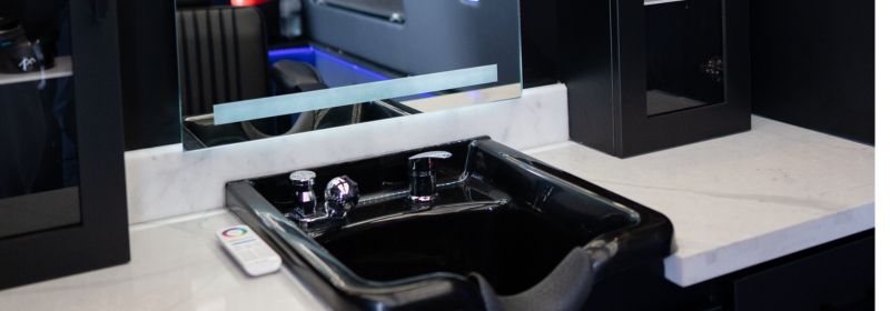 Black barber shampoo sink set into a marble countertop with a wall-mounted mirror inside the Montana Fades Sprinter mobile barbershop in Oakville, Ontario.